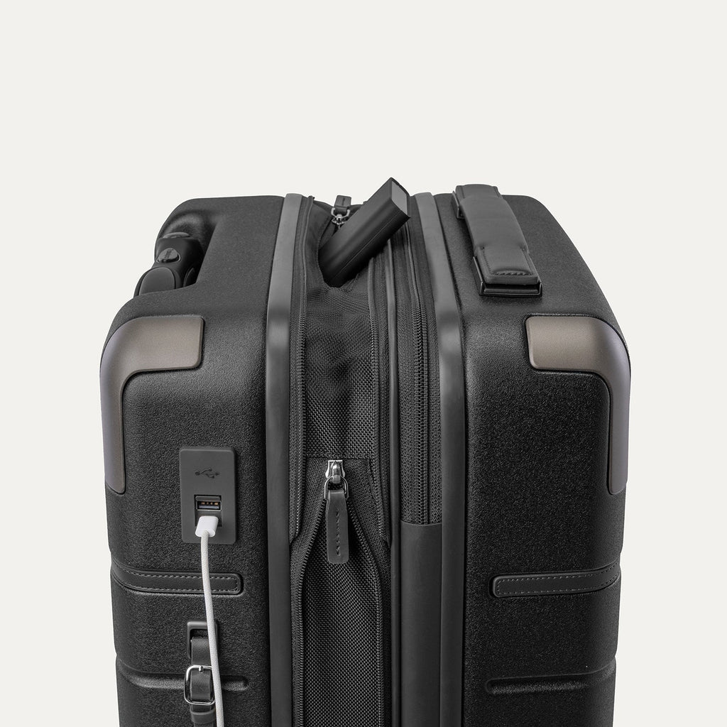 Charging cable plugged into the external USB port on the Travelpro Platinum Reserve Compact Cabin Hardshell Spinner in Black Dust