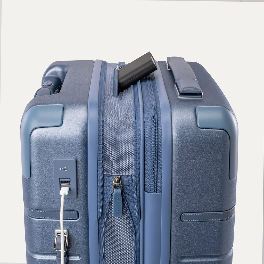 Charging cable plugged into the external USB port on the Travelpro Platinum Reserve Compact Cabin Hardshell Spinner in Steel Blue