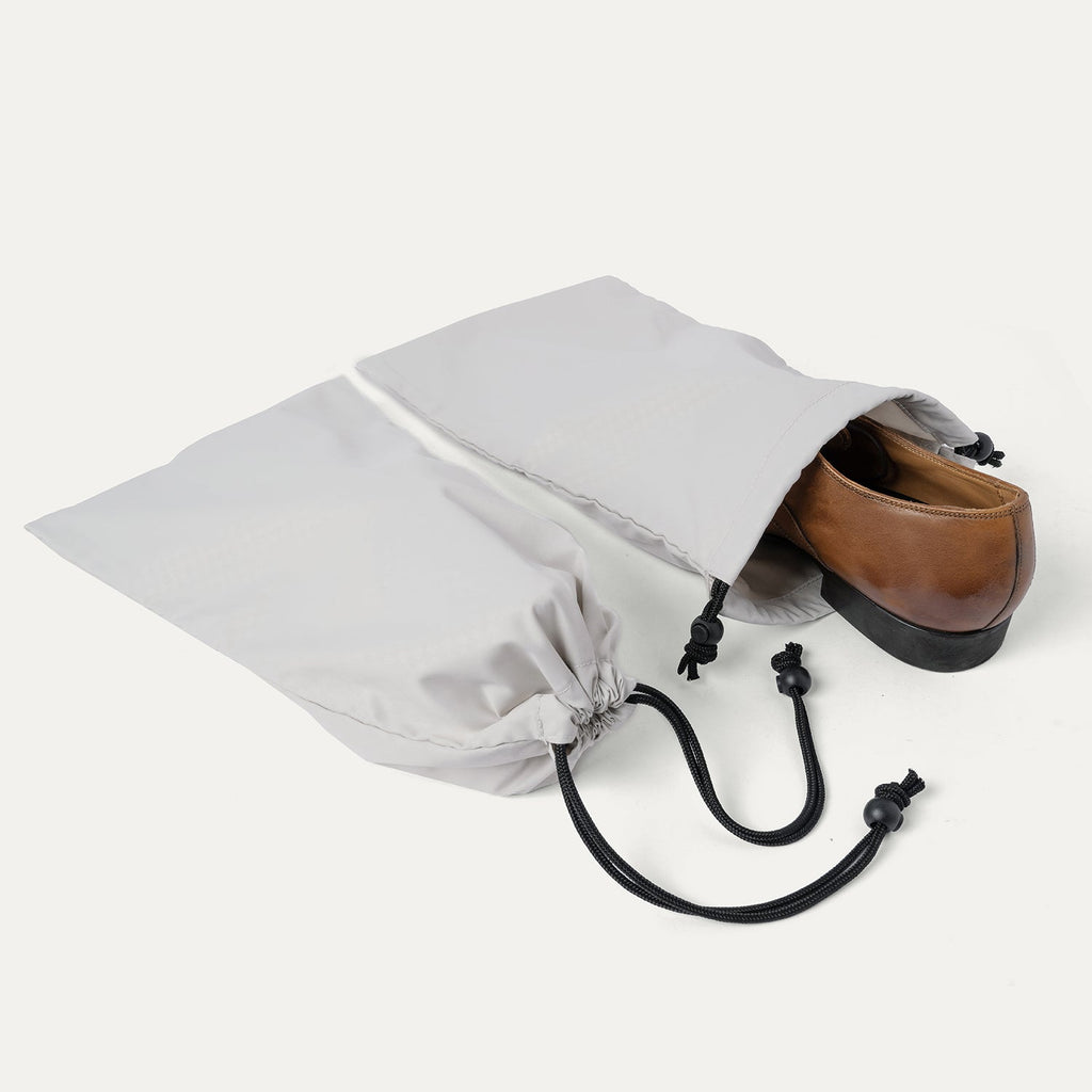 Drawstring shoe bag included with the Travelpro Platinum Reserve Large Check-In Hardshell Spinner in Black Dust, shown holding a pair of shoes