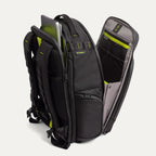 Three‑quarter rear view of the Travelpro Altitude Large Backpack in Neon Shadow, showing black textured exterior with neon yellow accents, open main compartment with gray lining, and multiple zippered pockets against a light background.