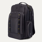 Three‑quarter front view of the Travelpro Altitude Large Backpack in Neon Shadow, showing black textured exterior with neon yellow stitching accents, multiple zippered compartments, and an iPhone in the front pocket against a light background.
