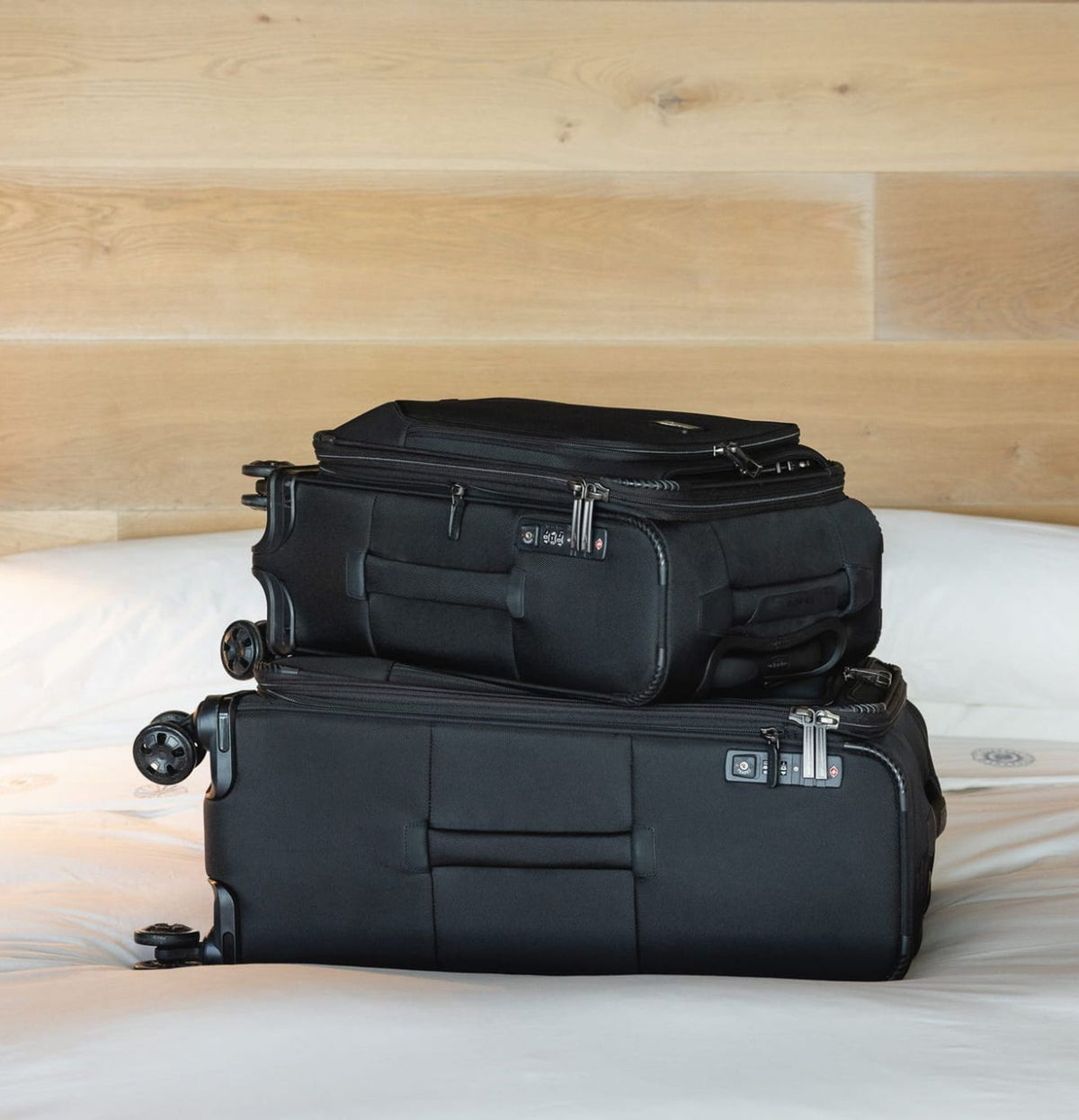 Two black Travelpro Crew Classic softside suitcases stacked on a hotel bed